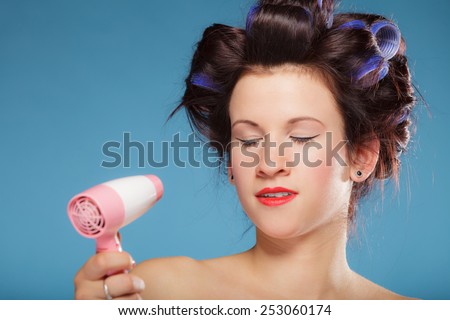 Young woman preparing to party having fun, funny girl styling hair with hairdreyer retro style on blue