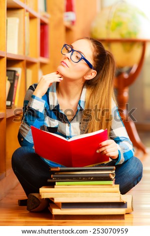 Education school concept. Clever female student long hair girl blue glasses sitting on floor in college library with stack books. Indoor