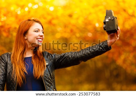 fashionable redhair tourist girl young woman taking self photo picture with old vintage camera. Beauty autumn park, golden leaves background