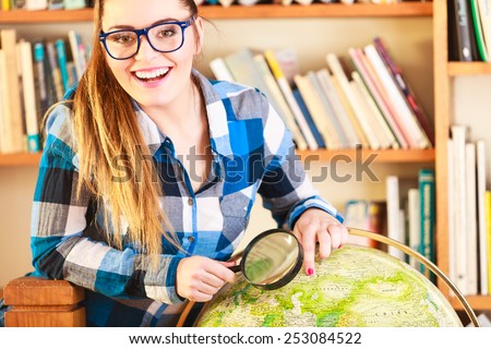 Education travel and geography concept. Young clever woman female student in blue glasses in library with globe and magnifying glass