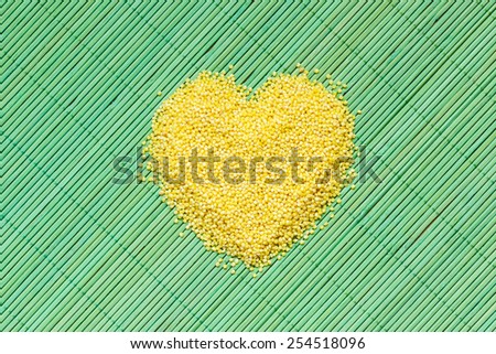 Dieting healthcare concept. Millet groats heart shaped on green straw mat surface. Healthy food non gluten grain.