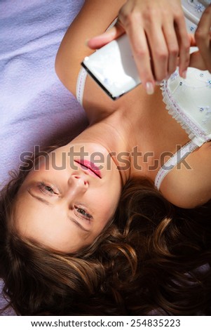 Texting and calling concept. Beauty young long haired woman lying on bad holding smartphone and texting.