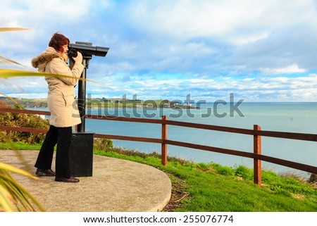 woman looking through sightseeing binoculars tourist telescope overlooking the ocean landscape, Church Bay Ireland Europe