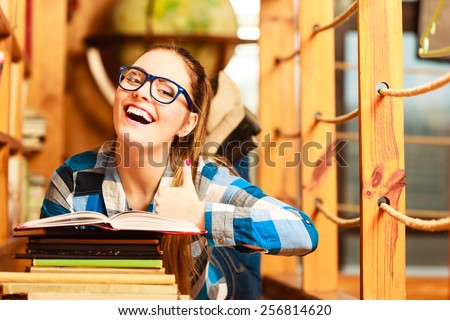 Education school concept. Clever female student girl in blue glasses lying on floor in college library with stack books reading. Indoor
