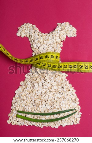Diet healthy food slim body concept. Female dress shape made from oatmeal vegetables with measuring tape around thin waist on red
