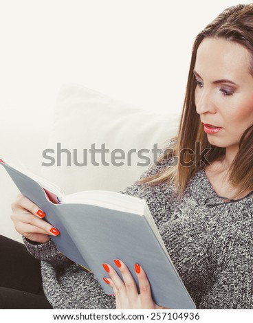 Leisure, education, literature and home concept - Woman sitting on couch reading book at home