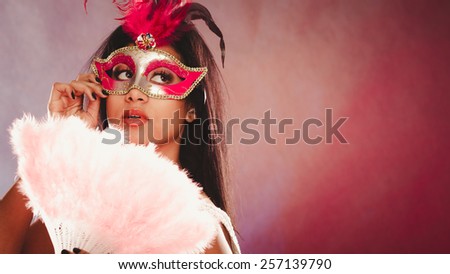 Holidays, people and celebration concept. African woman with carnival venetian masks holding feather fan in hand over festive background.