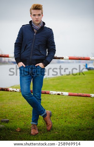 Autumn fashion. Young handsome man model in full length casual style hair styling outdoor against overcast sky, cold autumnal foggy day