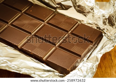 Sweet food. Dark chocolate bar in opened silver foil wrapping on wooden table.
