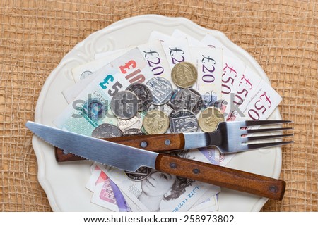 Cost of living, price of food and eating wealth concept. British money on kitchen table, coins and banknotes on plate.