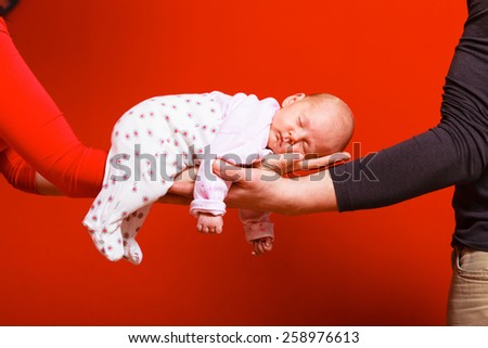 Parenting family and love concept. one month old baby girl sleeping in the comfort of parents arms, red background