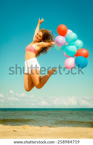 Summer holidays, celebration and lifestyle concept - beautiful woman teen girl jumping with colorful balloons outside on beach
