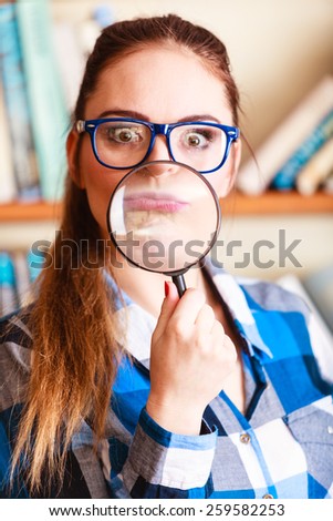 Investigation exploration education concept. Closeup funny student girl in library, woman in eyeglasses holding magnifying glass loupe
