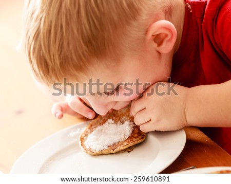 Little funny boy eating with relish mael fried apple in pancake dough or apple fritters pancakes with icing sugar at home