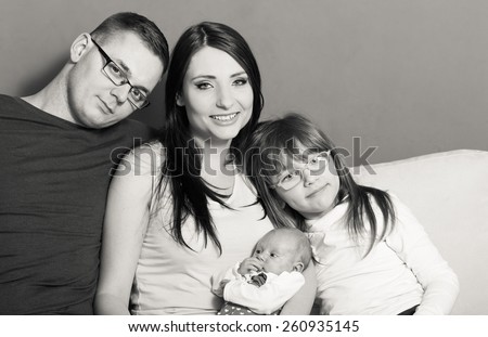 Parenthood and happiness concept. Young family mother father and child preschooler sitting on sofa with newborn baby girl at home. Black & white