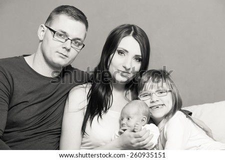 Parenthood and happiness concept. Young family mother father and child preschooler sitting on sofa with newborn baby girl at home. Black & white