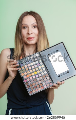 Cosmetic beauty procedures and makeover concept. Woman holds makeup professional palette. Make-up applying. Green background