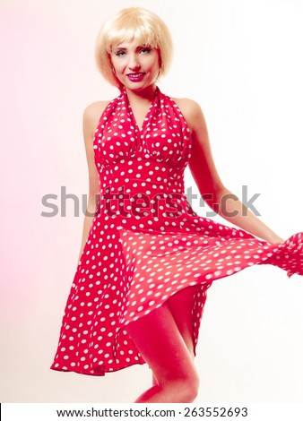 Vintage pinup style. Beautiful stylized young woman dancing. Attractive girl in blond wig and retro spotted red dress on pink. Disguise. Party. Studio shot.