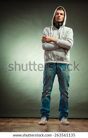 Music leisure youth concept. Young hooded man teen boy in full length with headphones on neck grunge background