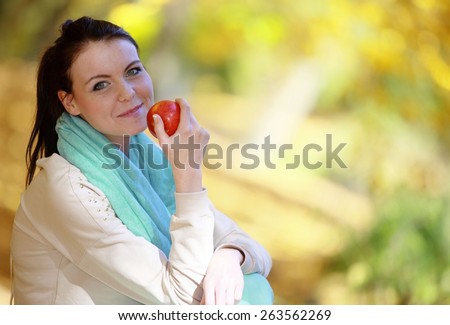 Fall lifestyle concept, harmony freedom. Casual young woman girl relaxing in autumnal park eating red apple. Golden colorful leaves background