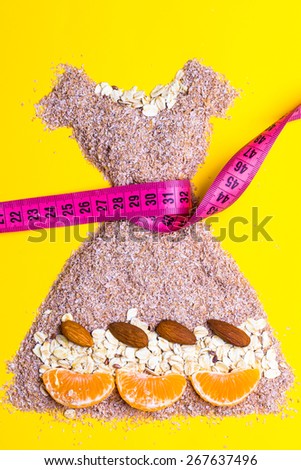 Dieting healthy eating slim down concept. Female dress shape made from cereal bran with measuring tape around thin waistline on yellow