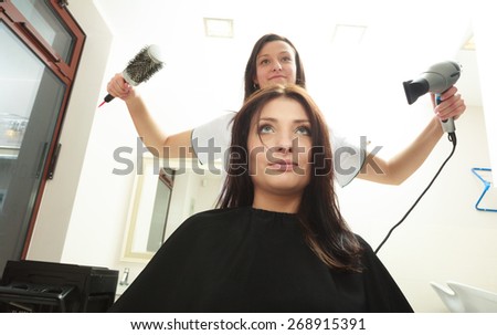 Brunette young woman girl with wet hair in hairdressing beauty salon. Hairstylist hairdresser with dryer and brush drying hair of female client.
