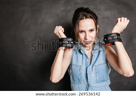Arrest and jail. Criminal woman prisoner girl showing leather handcuffs on gray. Punishment.