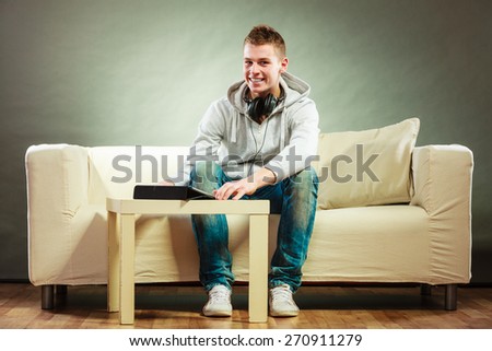 Modern technologies leisure and lifestyle concept. Young handsome man with headphones sitting on couch with tablet at home