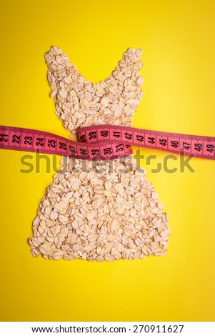 Dieting healthy eating slim down concept. Female dress shape made from oatmeal with measuring tape around thin waist on yellow