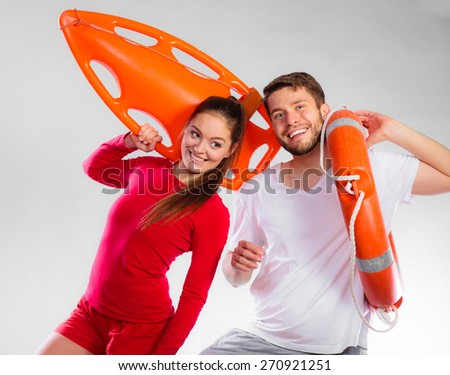 Accident prevention and water rescue. Young man and woman lifeguard couple on duty holding ring buoy float lifesaver equipment having fun on gray