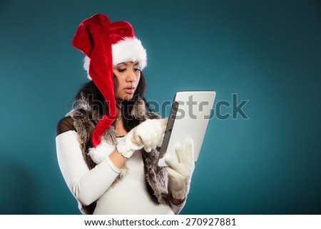 Technology internet and christmas time concept. Mixed race girl in santa claus helper hat using tablet touchpad on blue