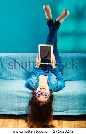 Modern technology education internet concept. Fashion young woman in glasses with tablet relaxing on blue color unusual view