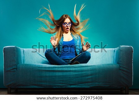 Technology internet concept. Fashion woman wearing denim sitting with tablet on couch hair blowing face expression blue color