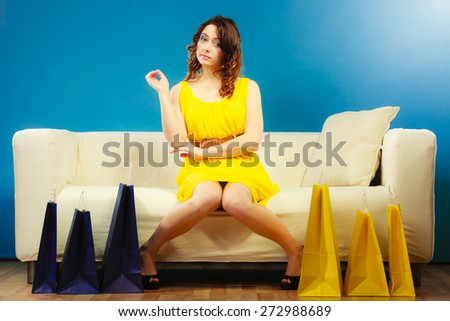 Buying retail sale concept. Fashionable girl yellow dress high heels sitting on couch with shopping bags on blue