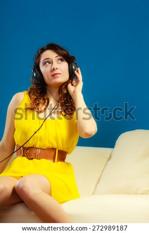 Young people leisure relax concept. Teen cute girl yellow dress in big headphones listening music mp3, sitting on couch relaxing on blue