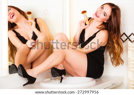 Applying make up concept. Beautiful woman with makeup brush in front of mirror in bathroom. Indoor.