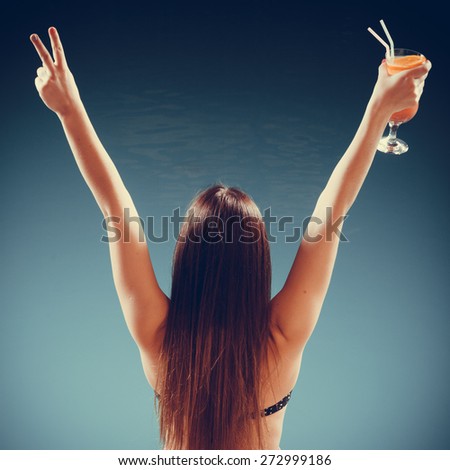 Spa relax and holidays concept. Happy woman in swimsuit back view. Fit female body, girl long hair at poolside with cocktail glass arms raised up in celebration
