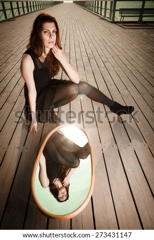 Solitude loneliness concept. Thoughtful young woman looks at the reflection in the mirror outdoors on pier