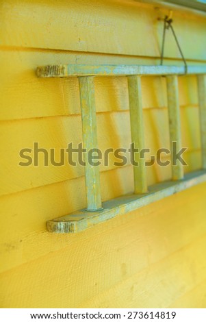 Wooden old  ladder hanging on yellow house wall