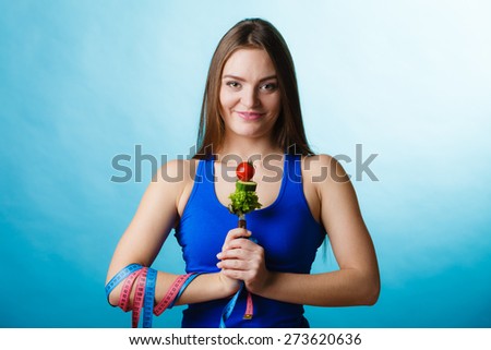 Weight loss and dieting concept. Sporty girl fitness woman holding fork with vegetarian food on blue background in studio.
