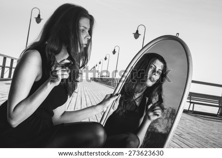 Solitude loneliness concept. Thoughtful young woman looks at the reflection in the mirror outdoors bw photo