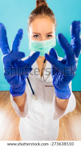 Preparing to surgery, protective equipment concept. Young woman doctor in face surgical mask and medical gloves on blue background