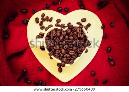 Coffee klatsch java concept. Heart shaped white cup filled with roasted coffee beans on red cloth background