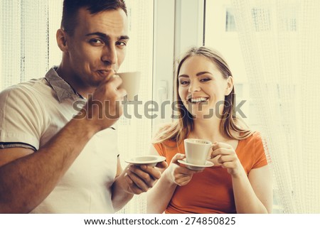 Happiness and healthy relationship concept. Attractive couple drinking tea or coffee together at home, man and woman holding cups with hot beverage at home