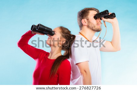 Young man and woman lifeguards on duty or tourist couple looking through binocular studio shot on blue