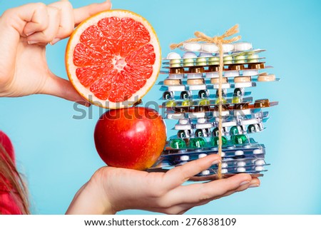 Health and balanced diet concept. Choice between two sources of vitamins - pills or fruits. Closeup female hand holding stack of drugs apple and grapefruit on blue.