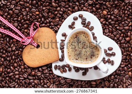 Coffee time concept. Heart shaped cup with cappuccino mocha and cookie gingerbread on coffee beans background. Top view