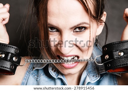 Arrest and jail. Criminal woman prisoner girl biting chain of leather handcuffs on gray. Punishment.