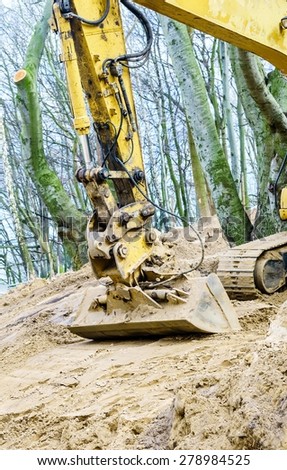 Yellow excavator dig digging trench on construction site in forest among trees. Devastation destruction of natural environment.