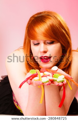 Candy addiction. Multi colored jelly sweets in red haired woman hands. Studio shot.